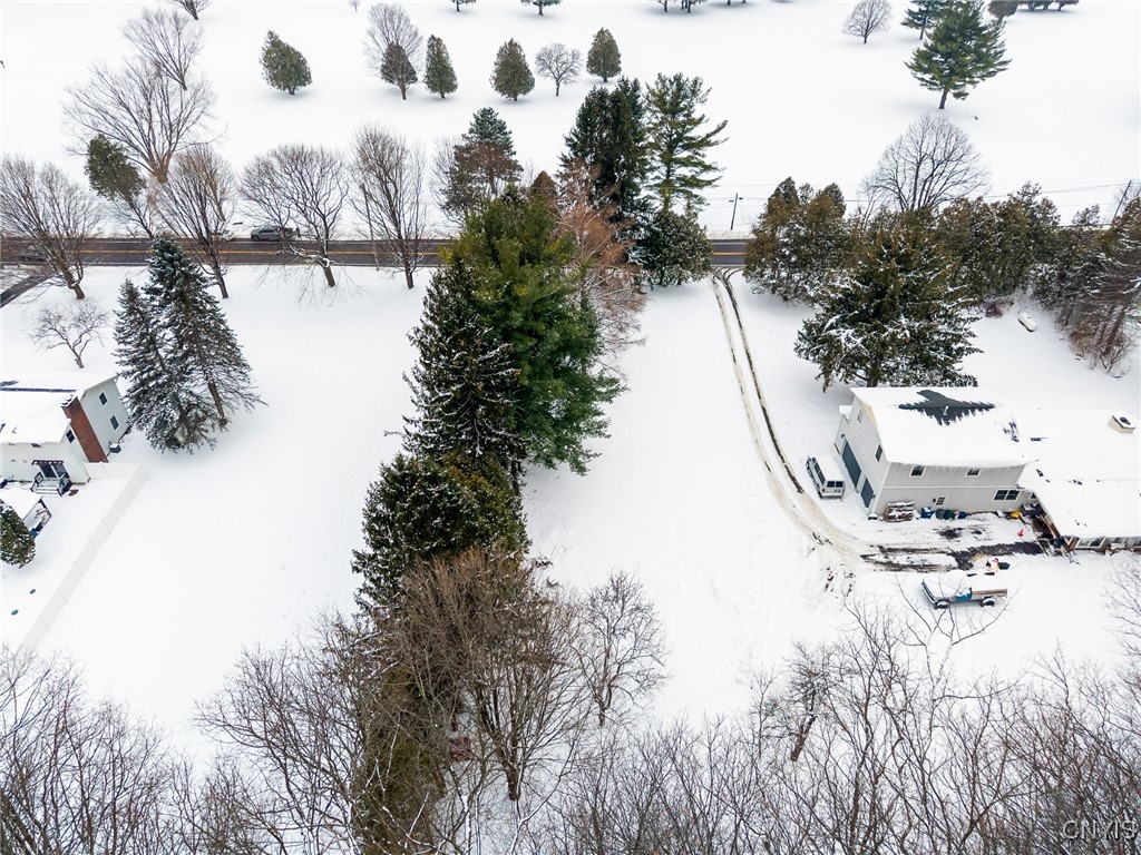 Snow-covered property with a two-story house, tree-lined lot, and driveway leading to the road.