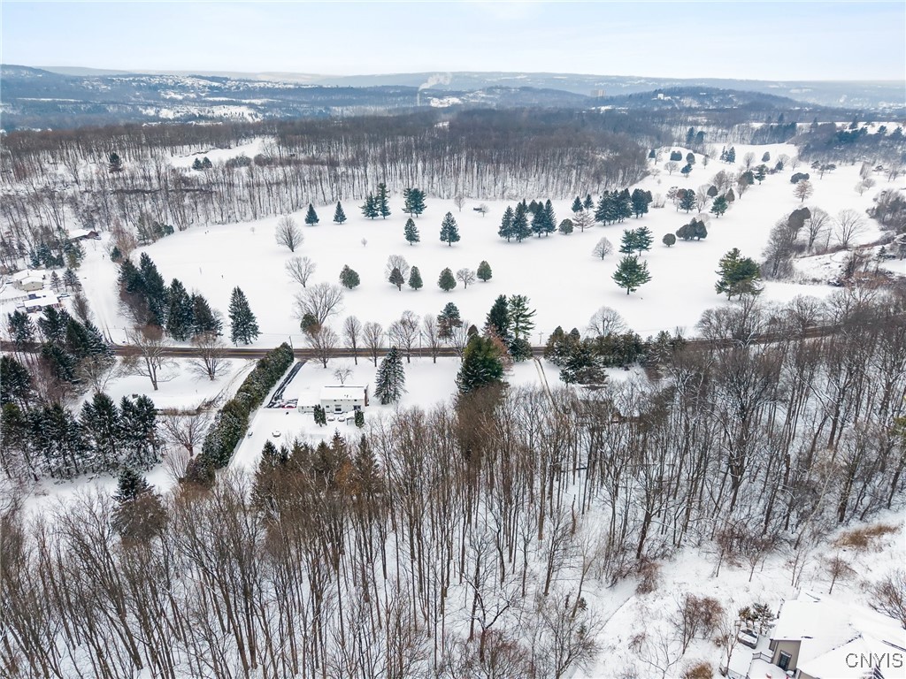Aerial view of a house and snow-covered grounds bordered by woods, with a broad open field beyond.