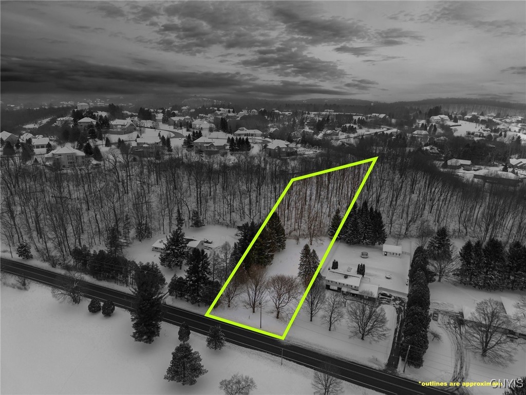 Aerial view of a snow-covered lot outlined in green beside a road and wooded area.