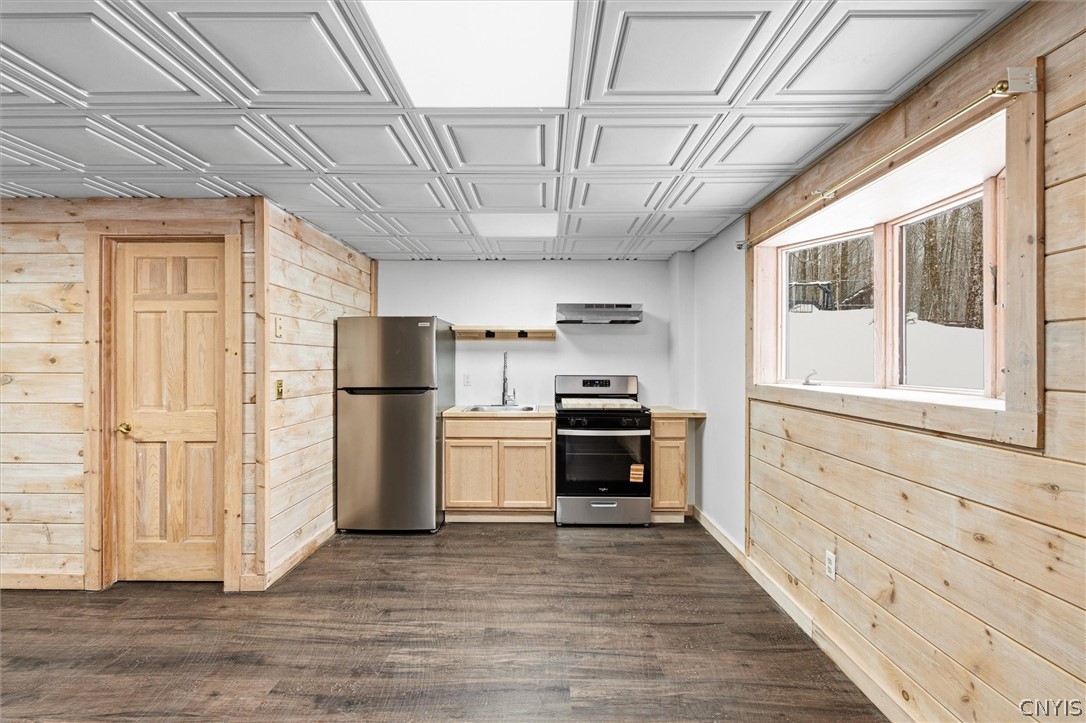 Compact kitchen with light wood cabinetry, stainless steel appliances, and a window overlooking snow.