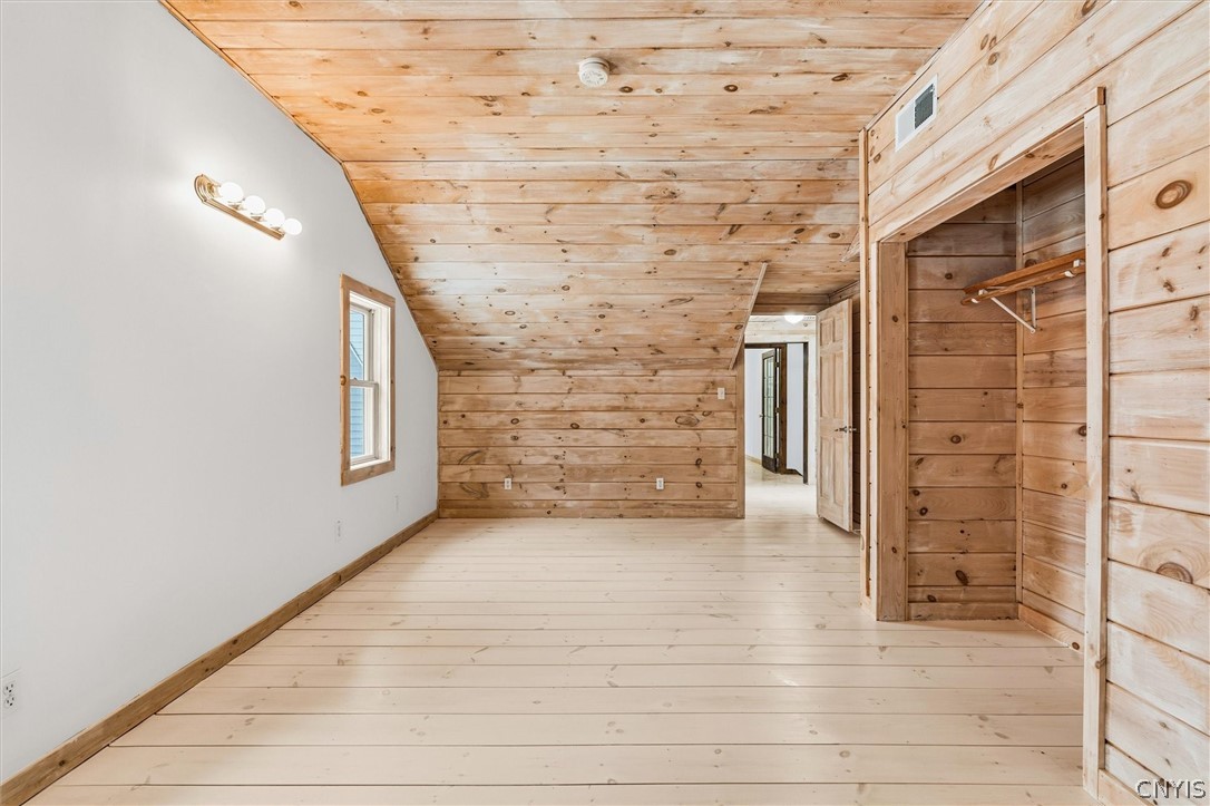 Vacant room with wood-plank walls and sloped ceiling, an open closet, and pale wood flooring.