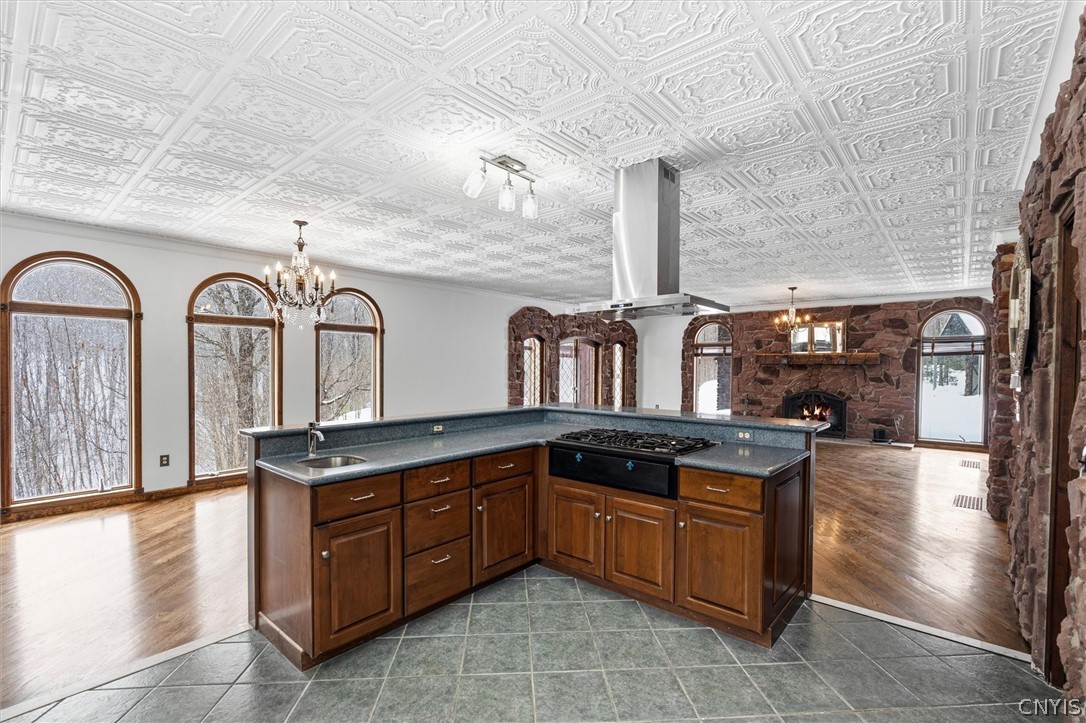 Kitchen with a large wood-cabinet island, ornate ceiling tiles, arched windows, and a stone fireplace.