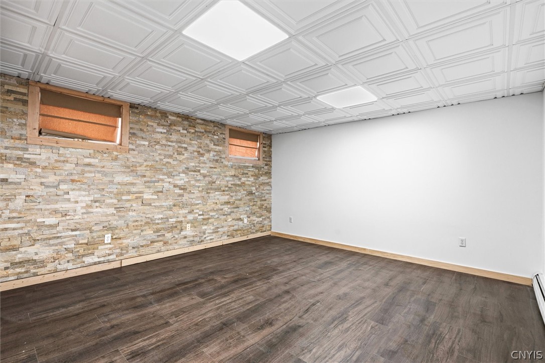 Empty room with a stacked-stone accent wall, dark flooring, and a patterned white ceiling.