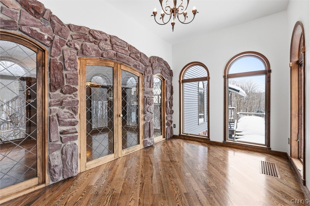 Empty room with hardwood floors, a stone accent wall, and arched windows overlooking snow.