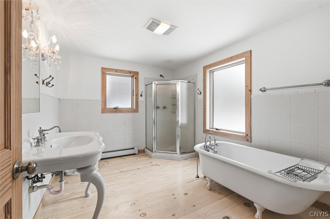 Bathroom with a clawfoot tub, corner shower, pedestal sink, and pale wood floors.