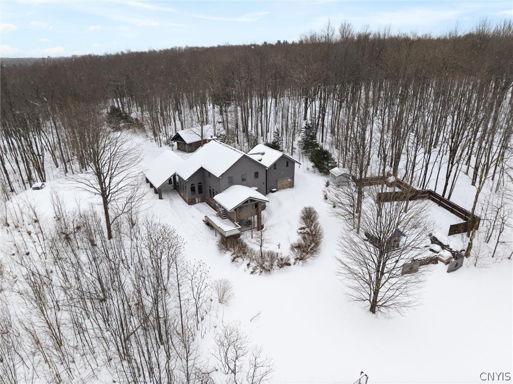 Aerial view of a gray house and fenced yard surrounded by snowy, leafless woods.