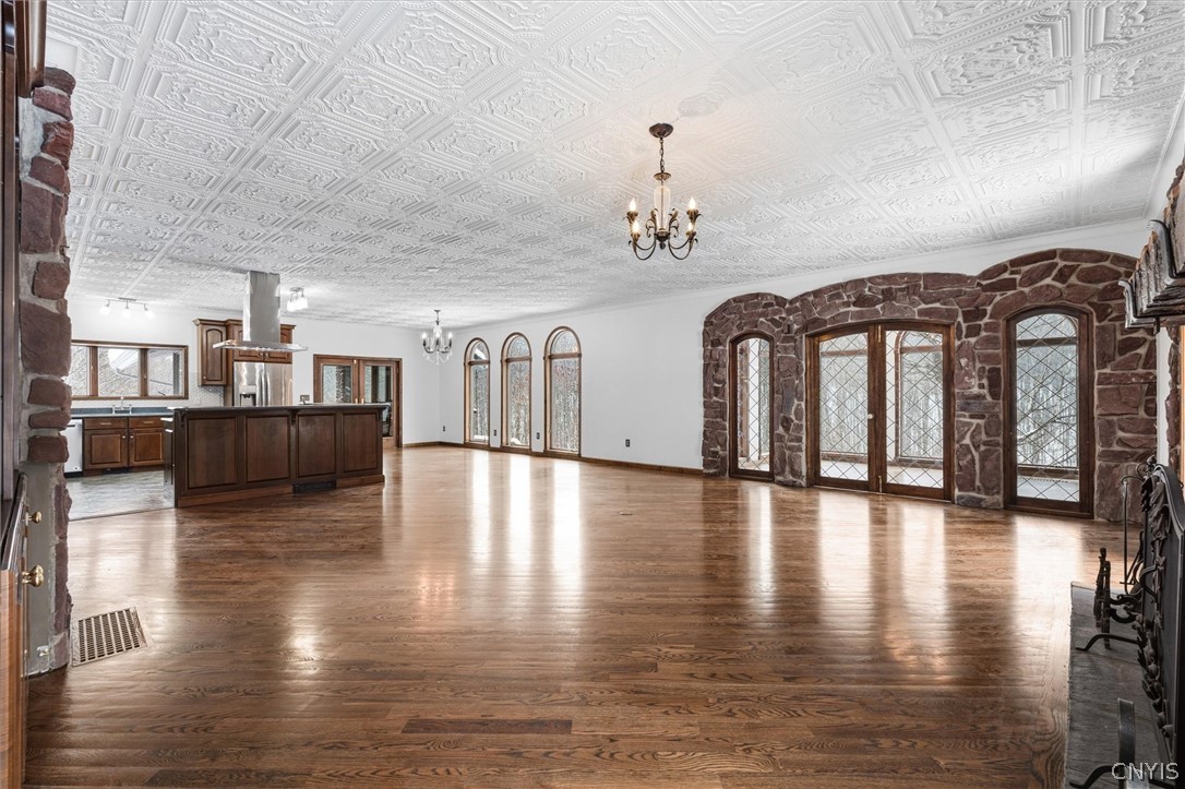 Vacant living area with ornate patterned ceiling, hardwood floors, and stone-framed leaded-glass doors.