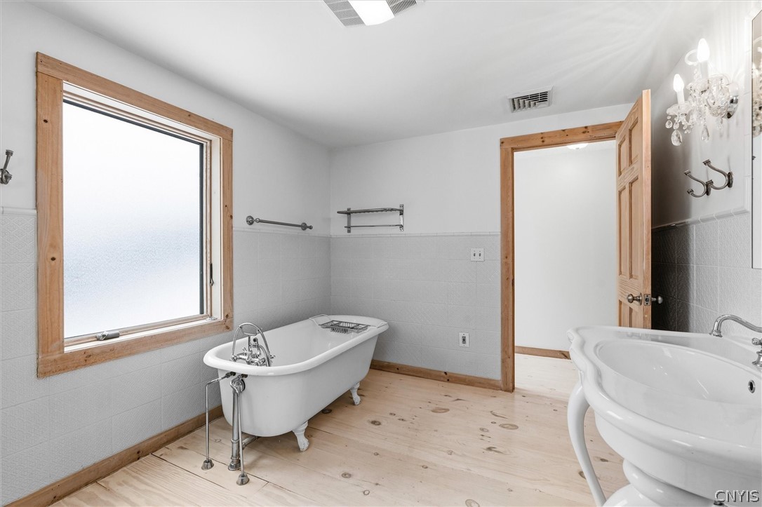 Bathroom with a clawfoot tub beneath a frosted window and a pedestal sink.
