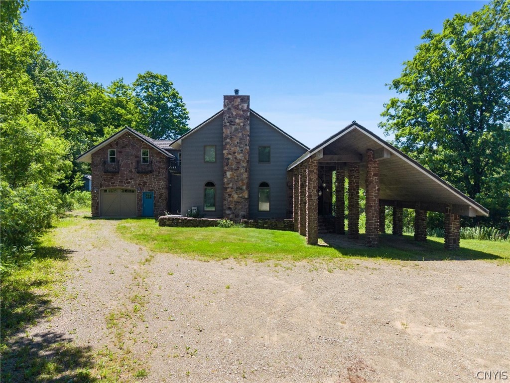 Home with a stone chimney, attached garage, and columned covered drive.