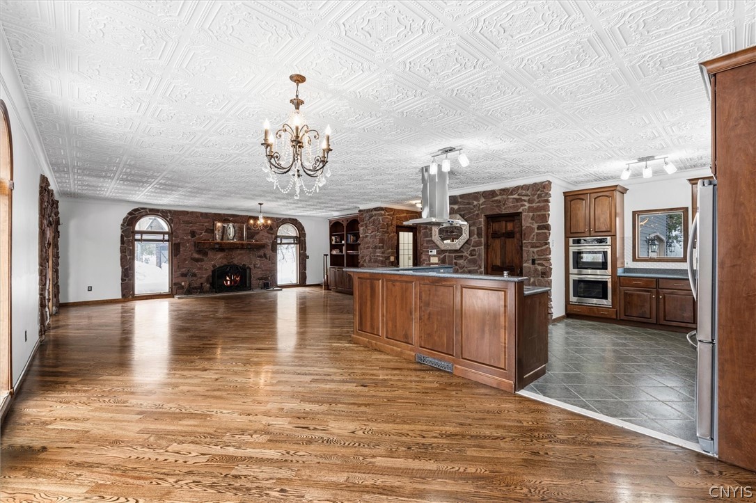 Open kitchen and living area with a wood island, stone fireplace, hardwood floors, and ornate ceiling.