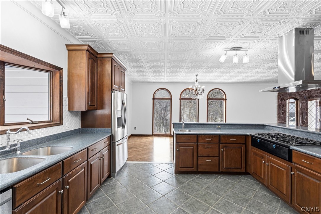 Kitchen with dark wood cabinetry, a cooktop island, ornate ceiling, and three arched windows.