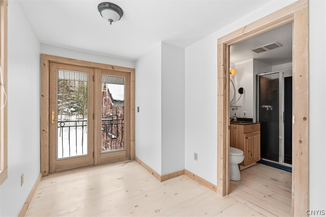 Empty room with pale wood floors, double glass doors, and an adjoining bathroom.