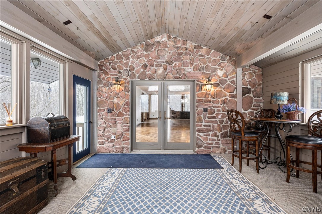 Entryway with a tall stone wall framing glass double doors beneath a vaulted wood-plank ceiling.
