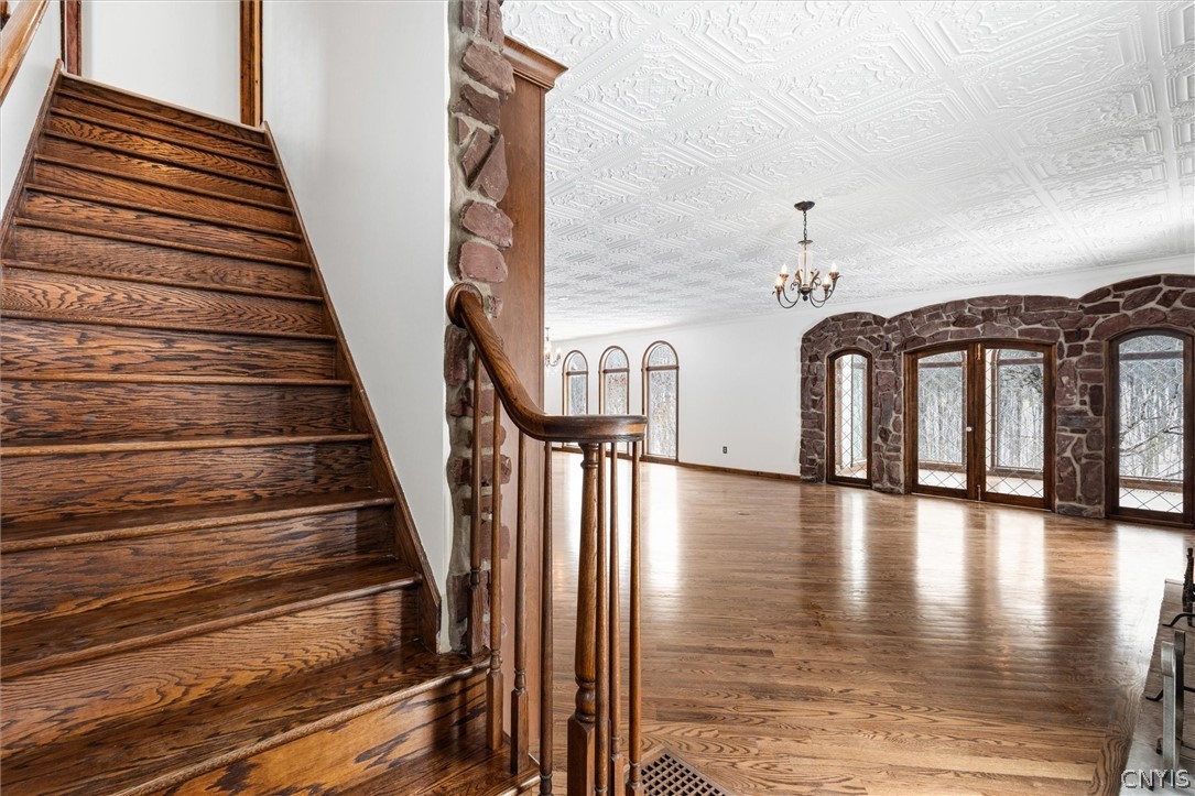 Vacant living room with a dark wood staircase, stone-framed arched windows, and an ornate ceiling.