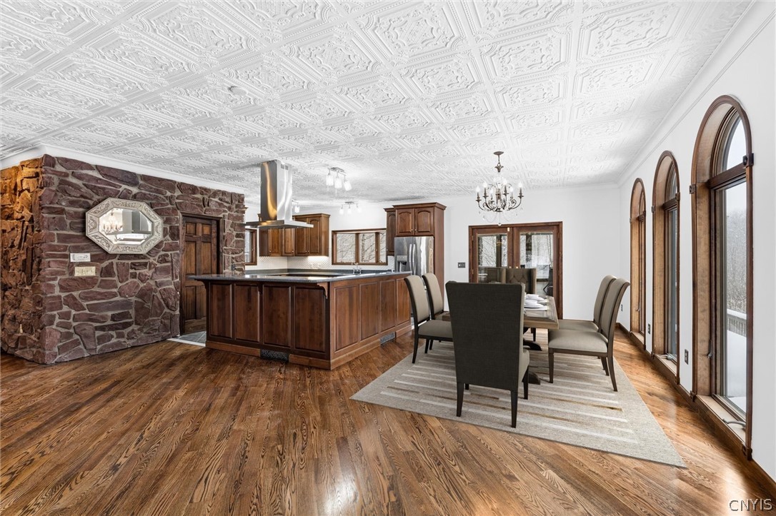 Kitchen and dining area with a dark wood island, stone wall, hardwood floors, and tall arched windows.