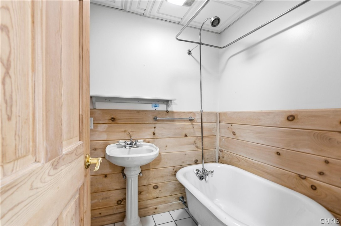 Bathroom with a white bathtub, overhead shower, pedestal sink, and light wood plank walls.