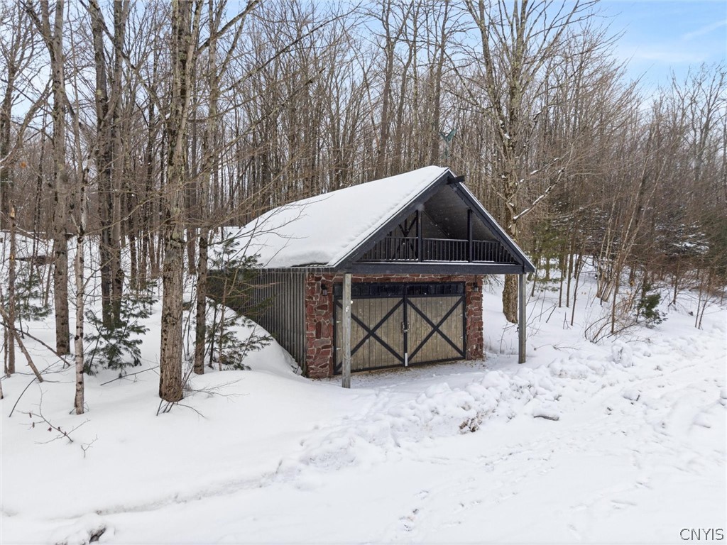 Detached stone-front garage with cross-braced doors and a loft balcony in a snowy wooded setting.