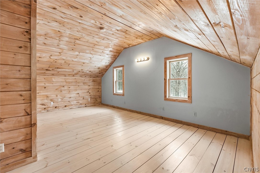 Unfurnished attic room with pale wood floors and a sloped, wood-paneled ceiling.