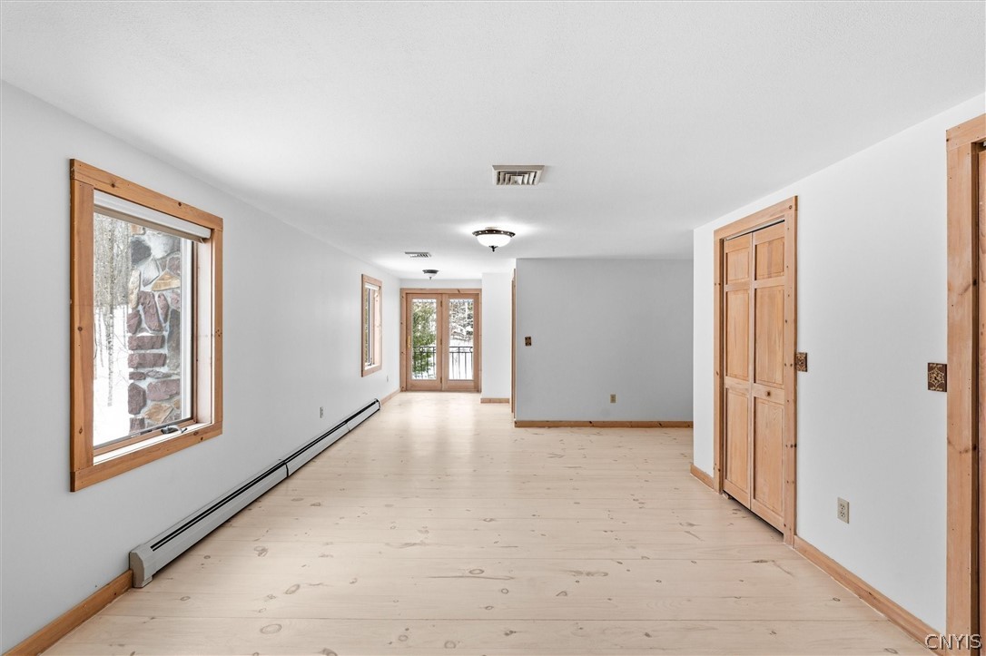 Empty room with pale plank floors, wood-trimmed windows, and glass doors at the far end.