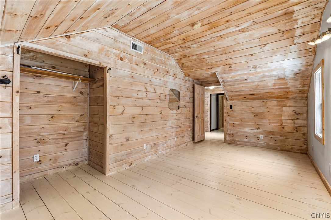 Empty wood-paneled attic bedroom with a sloped ceiling and open closet.