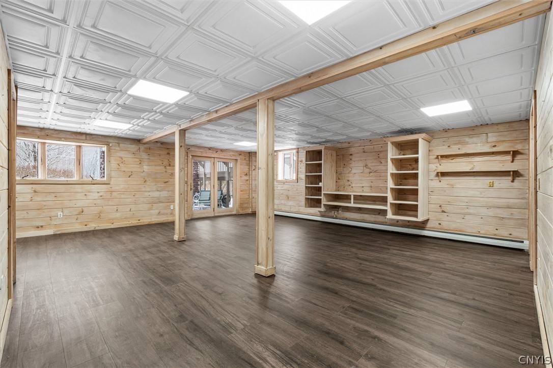 Vacant wood-paneled room with built-in shelving, support posts, and dark plank flooring.