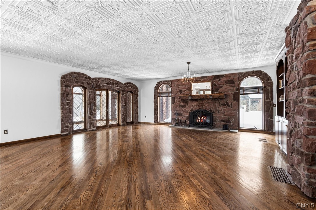 Empty living room with a stone fireplace, arched windows, polished hardwood floors, and an ornate pressed-tin ceiling.