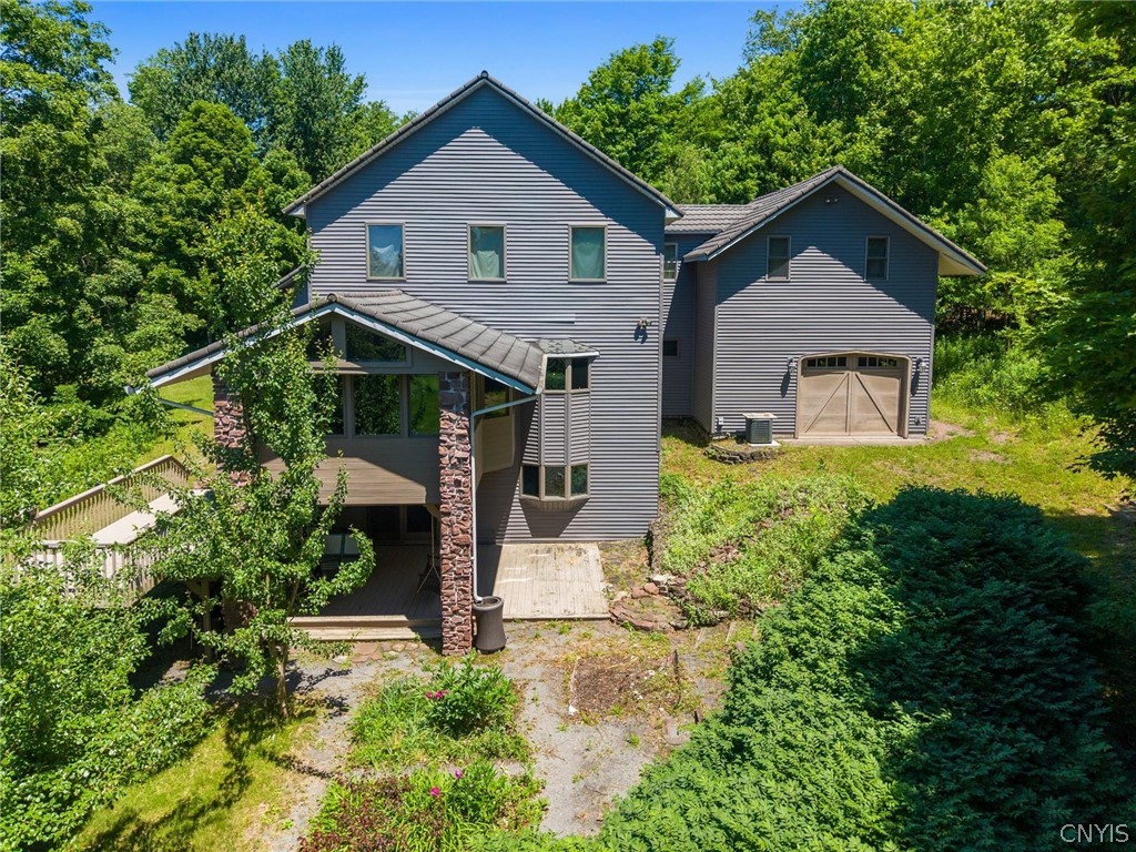 Gray two-story home with a covered rear porch and attached garage, surrounded by trees.