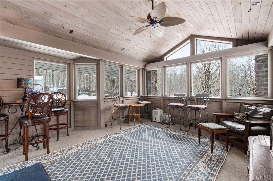 Furnished sunroom with a vaulted wood ceiling, large windows, and snowy woods outside.