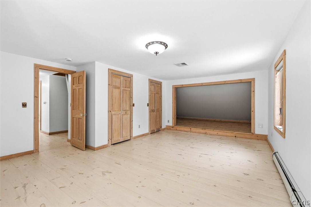 Vacant room with pale wood floors, natural wood trim, and a wide opening to an adjoining room.