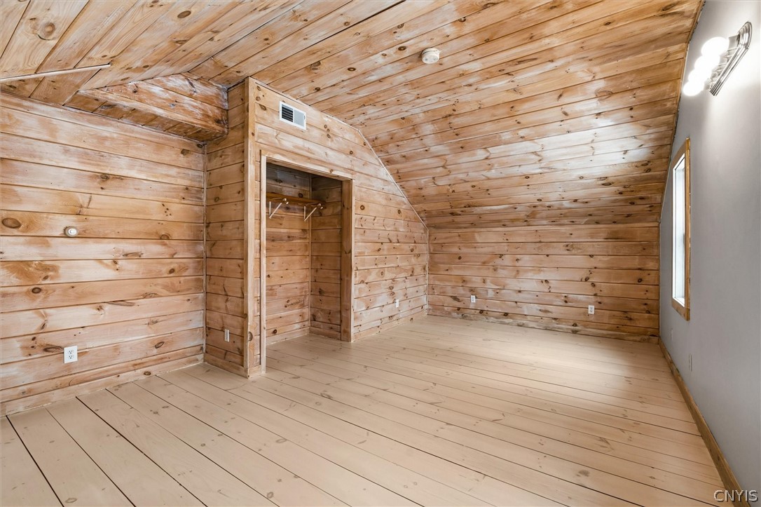 Vacant bedroom with wood plank walls and ceiling, an open closet, and a narrow window.