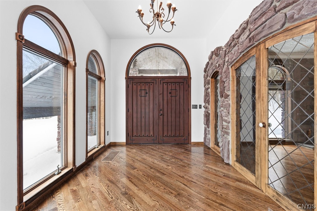 Entry foyer with arched windows, a wood double door, stone wall, and wide plank flooring.