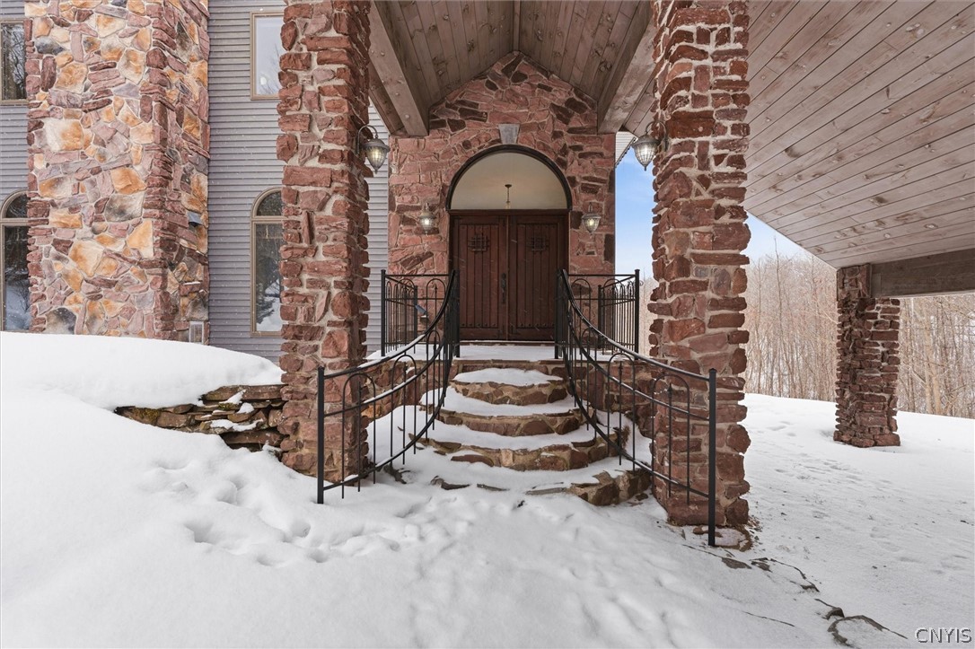 Stone home entrance with arched wooden double doors, covered porch, and snow-covered steps.