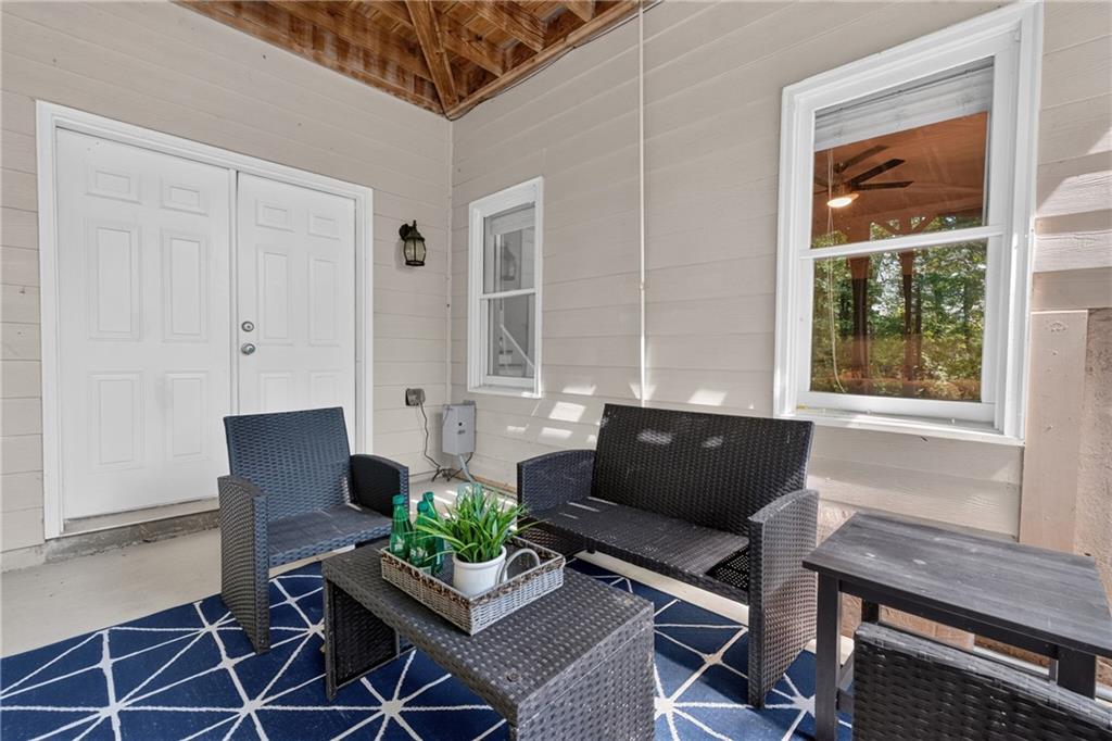 Covered porch with wicker seating, a potted plant, and a blue geometric rug.