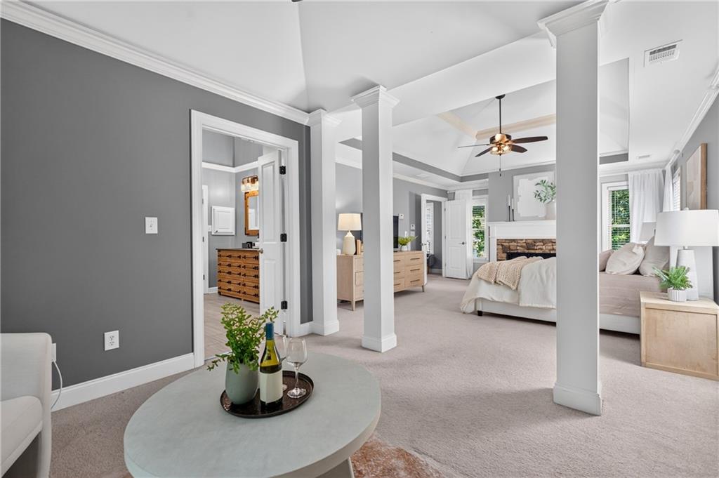 Staged bedroom with a fireplace, ceiling fan, and open sitting area framed by white columns.