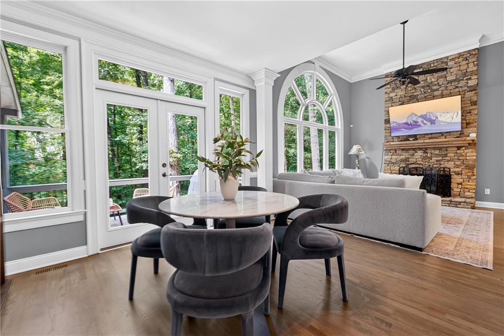 Dining area with a round table and dark chairs beside a living room with a stone fireplace.