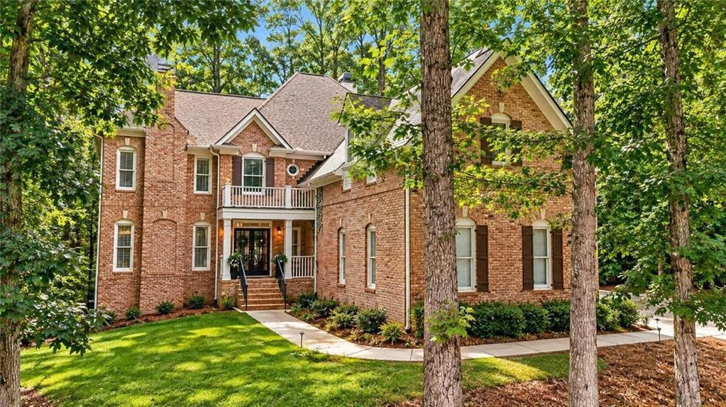 Two-story brick house with a covered porch, landscaped lawn, and mature trees.