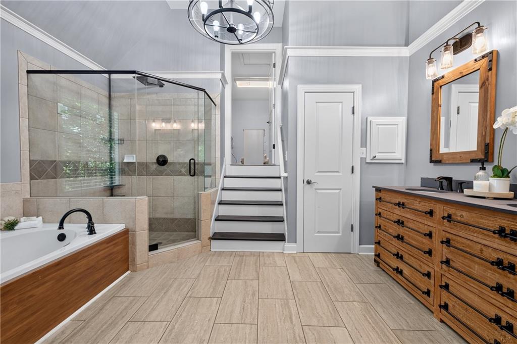 Bathroom with a glass-enclosed tiled shower, built-in tub, wood vanity, and stairs.
