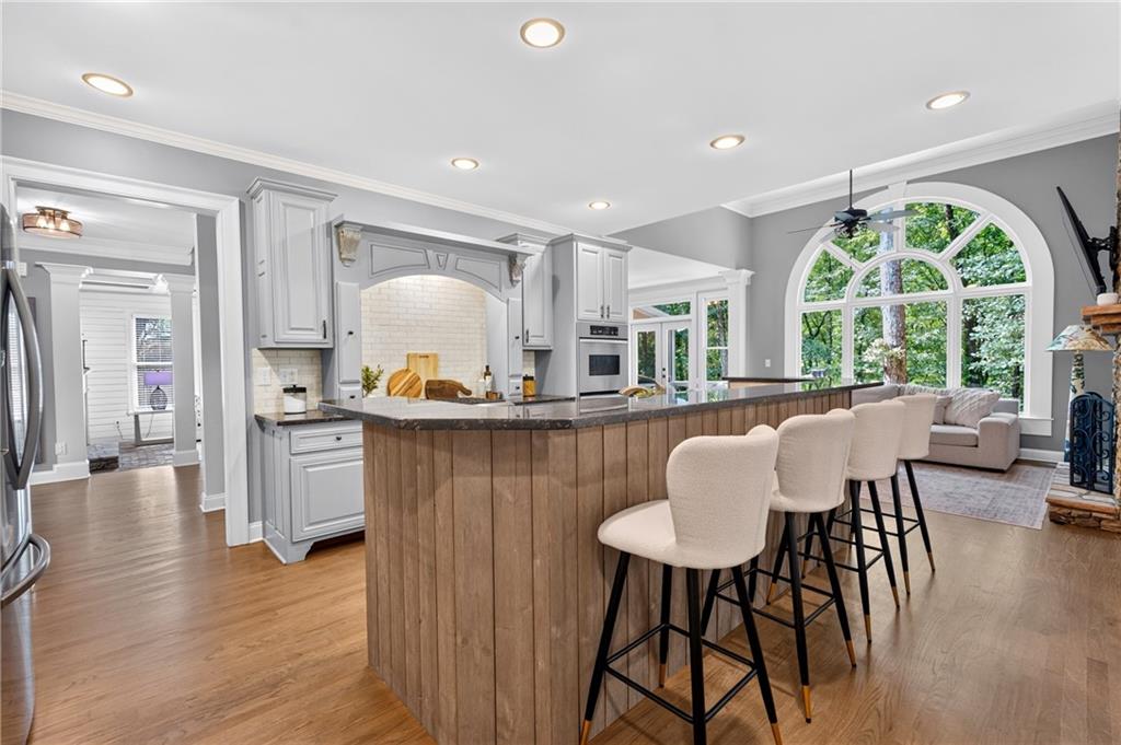 Open kitchen with a wood-paneled island, gray cabinets, and a large arched window overlooking trees.