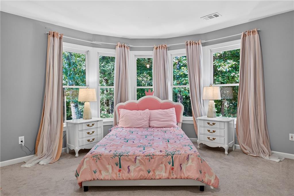 Bedroom with a pink floral bed, curved bay of tall windows, and views of leafy trees.