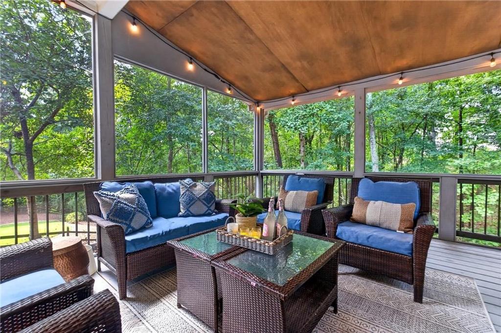 Screened porch with blue-cushioned wicker seating and a wooded view.