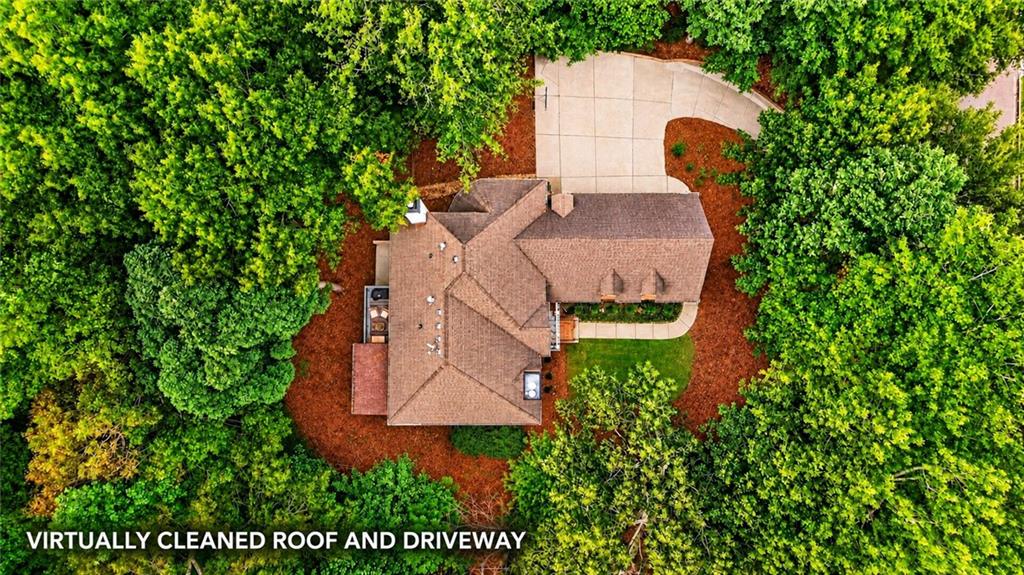 Aerial view of a home surrounded by dense trees, with a large paved driveway.