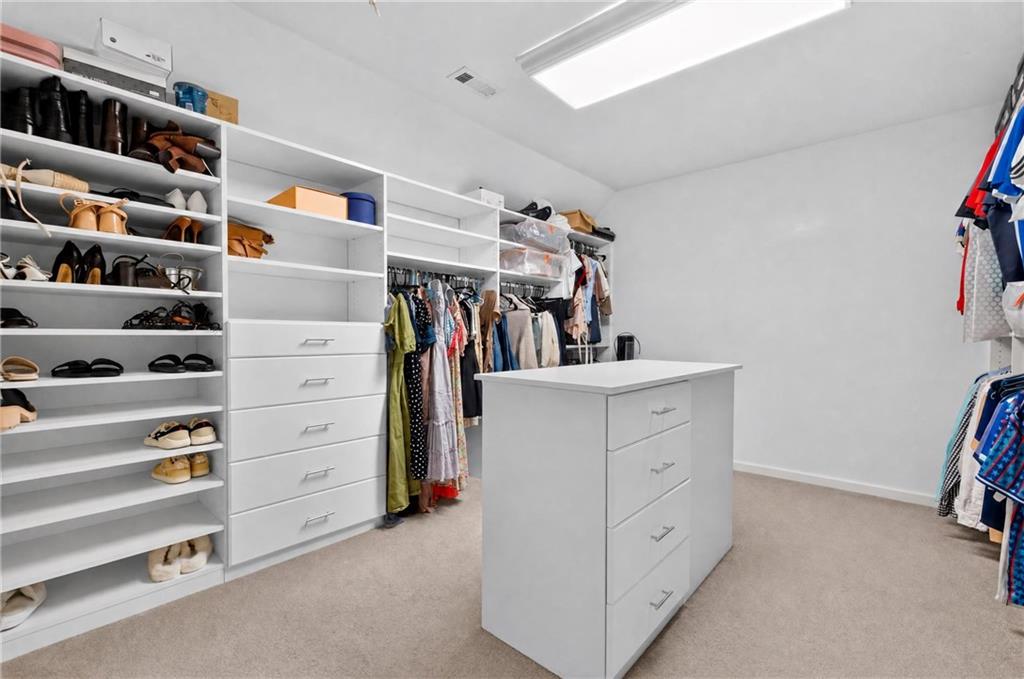 Walk-in closet with built-in shoe shelves, hanging clothes, and a central drawer island.