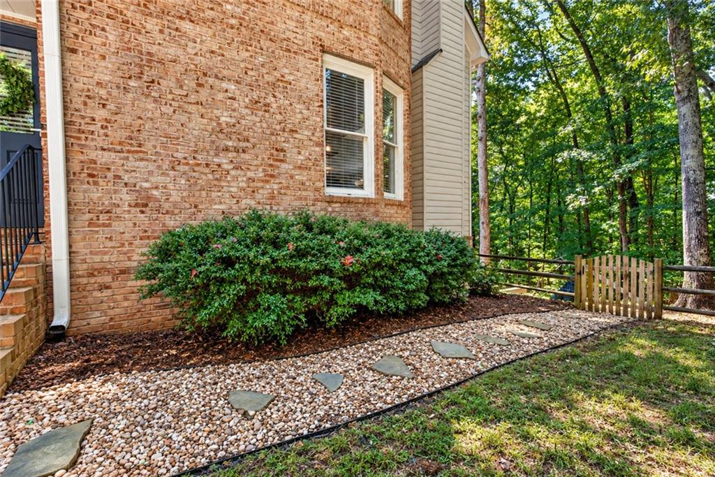 Brick house beside a pebble garden path and stepping stones, with trees beyond a small gate.