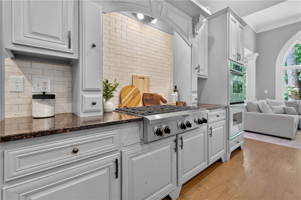 Kitchen with a stainless steel gas range, white cabinetry, and brick backsplash beside a living room.