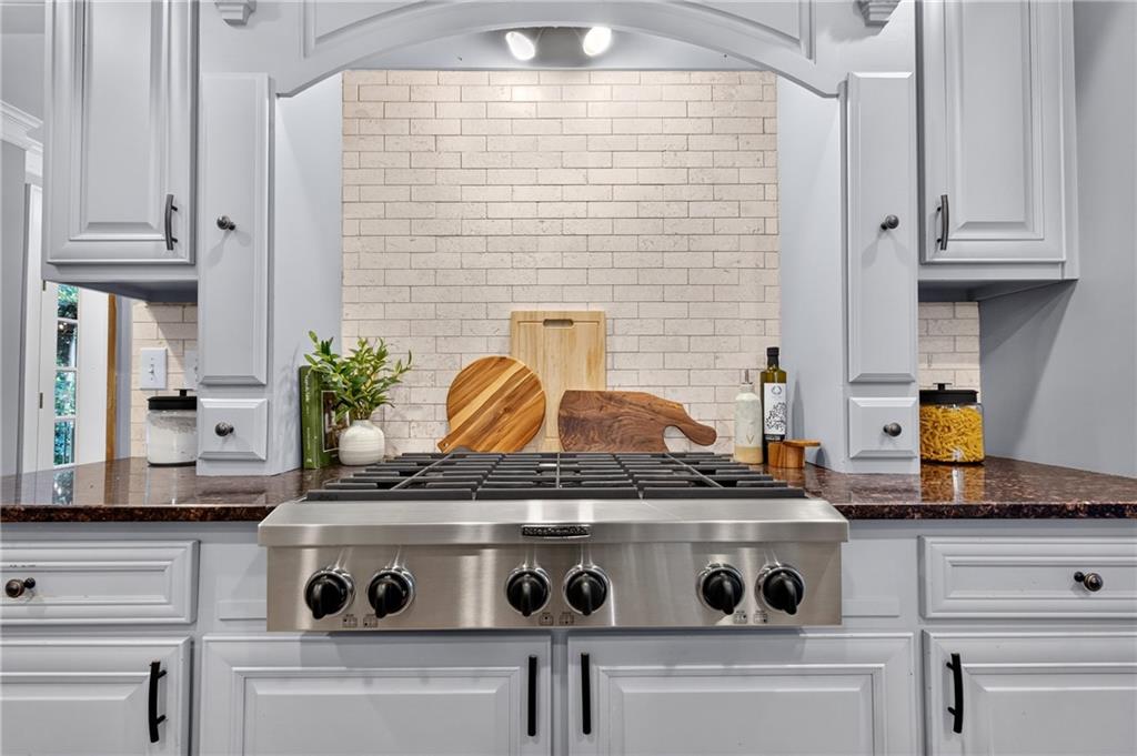 Kitchen with a wide stainless-steel gas range, white cabinetry, and pale brick backsplash.