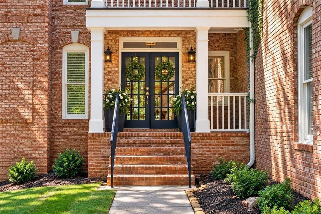 Red-brick home entrance with black double doors, wreaths, white columns, and brick steps.