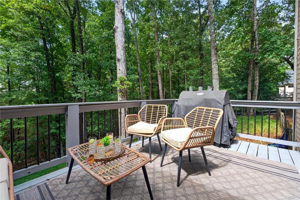 Outdoor deck with woven seating and covered grill overlooking leafy woods.