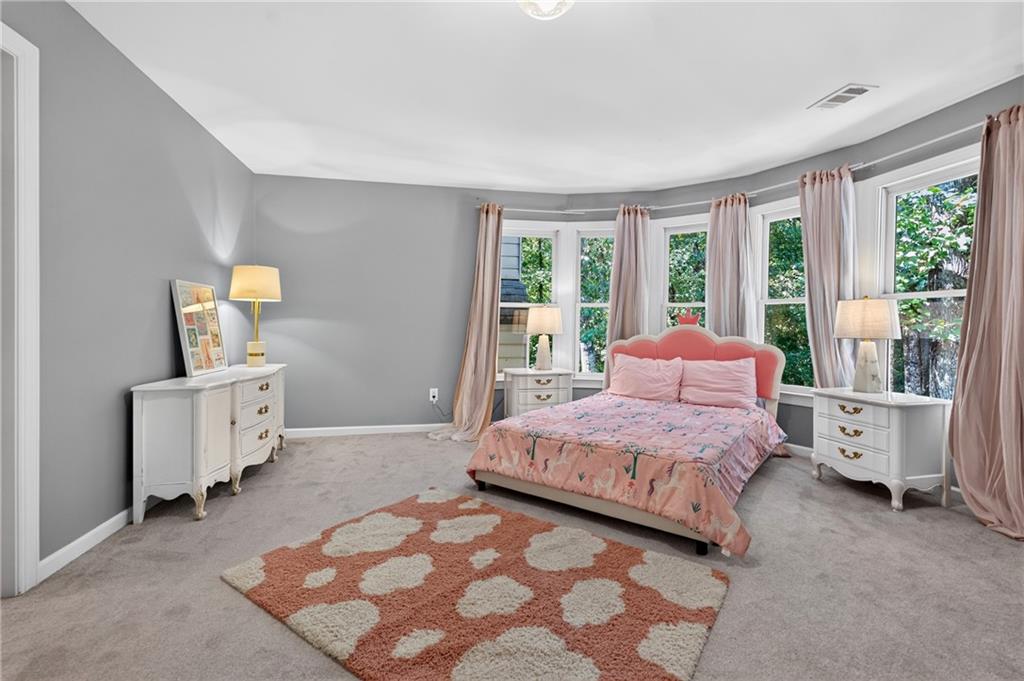 Bedroom with a pink floral bed in front of wide bay windows and a rust-colored patterned rug.