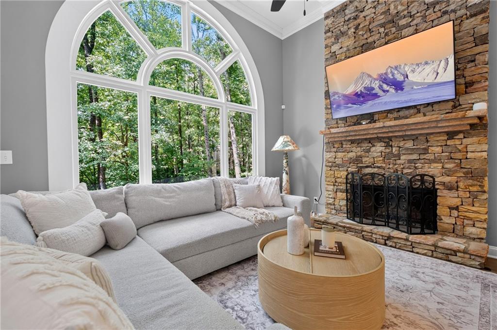 Living room with an arched window overlooking trees and a stacked-stone fireplace.
