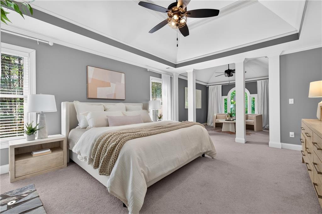 Staged primary bedroom with a white bed, tray ceiling and column-framed sitting area.
